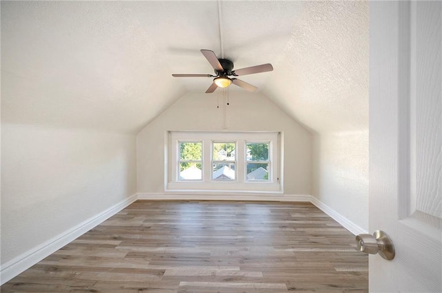 additional living space with vaulted ceiling, a textured ceiling, baseboards, and wood finished floors