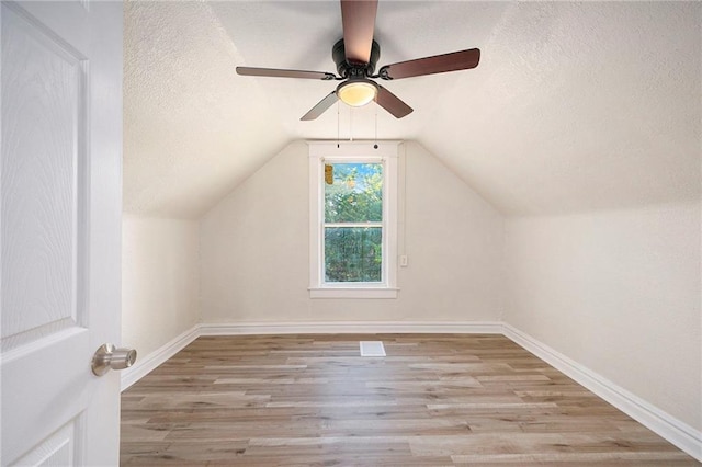 additional living space featuring a textured ceiling, wood finished floors, lofted ceiling, and baseboards