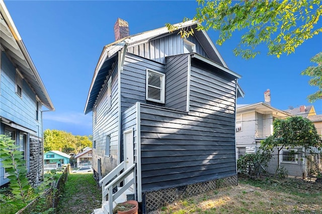 view of side of home featuring board and batten siding, fence, and a chimney