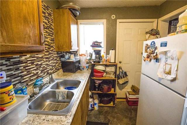 kitchen featuring a sink, light countertops, freestanding refrigerator, brown cabinets, and tasteful backsplash