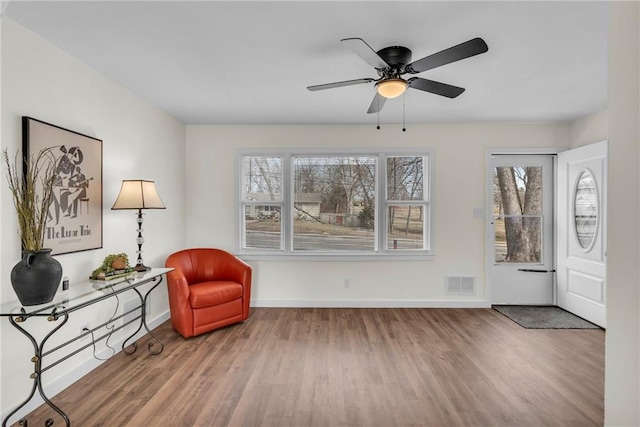 sitting room with ceiling fan, wood finished floors, visible vents, and baseboards