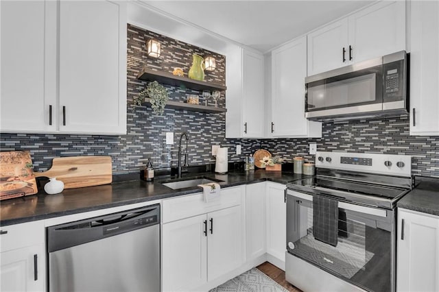 kitchen with stainless steel appliances, dark countertops, backsplash, white cabinetry, and a sink