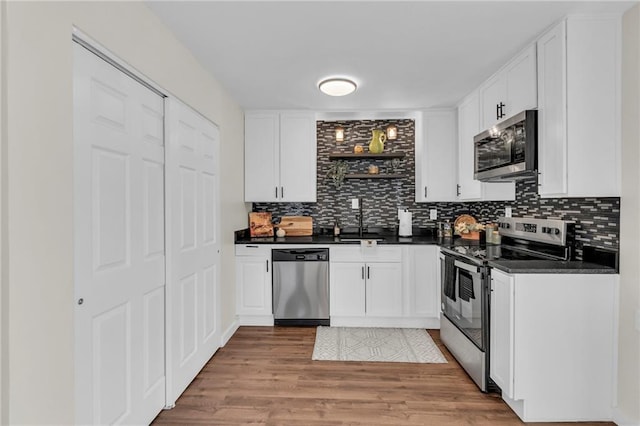 kitchen with dark countertops, appliances with stainless steel finishes, light wood-style floors, white cabinetry, and a sink