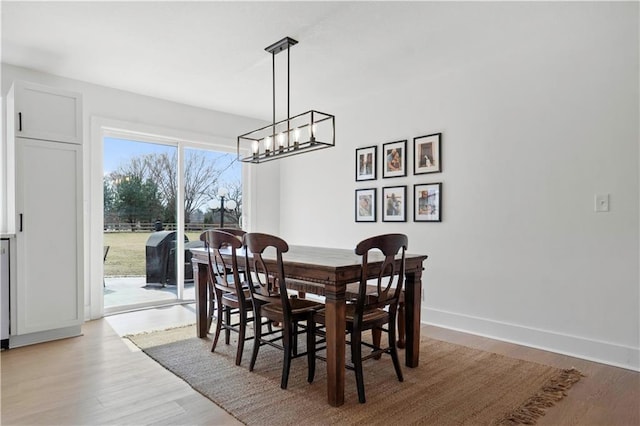 dining room featuring light wood-style floors, a notable chandelier, and baseboards