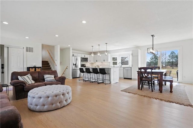 living room with a notable chandelier, recessed lighting, visible vents, light wood-style flooring, and stairs