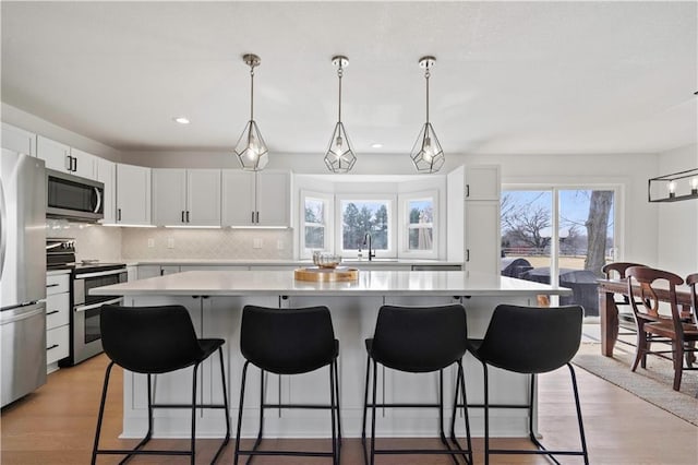 kitchen with a breakfast bar area, stainless steel appliances, light countertops, backsplash, and a sink