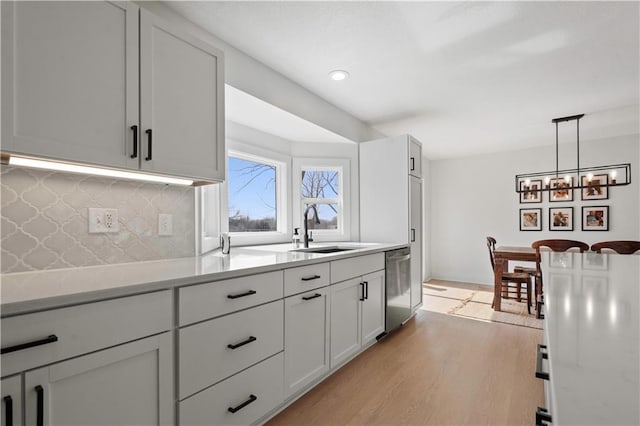 kitchen with tasteful backsplash, light countertops, light wood-style flooring, stainless steel dishwasher, and a sink