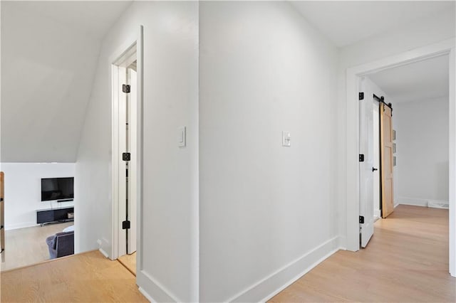 corridor featuring light wood-style floors, baseboards, and a barn door