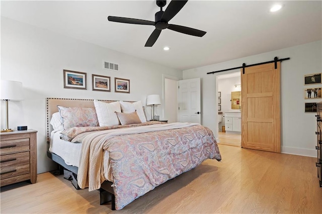 bedroom featuring ensuite bathroom, a barn door, recessed lighting, visible vents, and light wood-type flooring