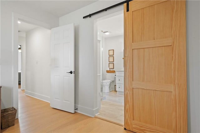 corridor featuring light wood finished floors, a barn door, and baseboards