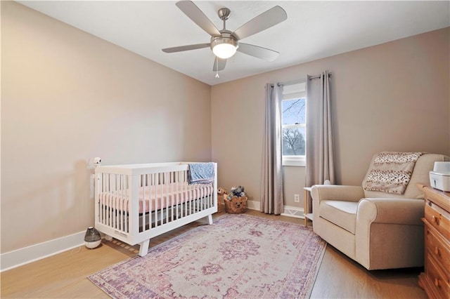 bedroom featuring ceiling fan, a crib, baseboards, and wood finished floors