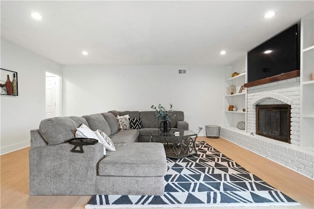 living area featuring built in features, recessed lighting, a brick fireplace, and wood finished floors