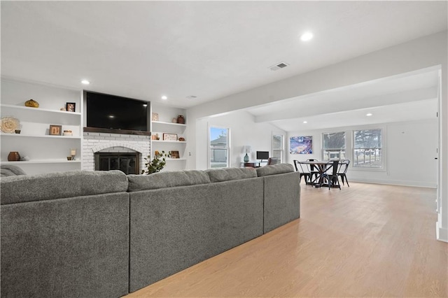 living room featuring built in shelves, recessed lighting, a fireplace, visible vents, and light wood finished floors