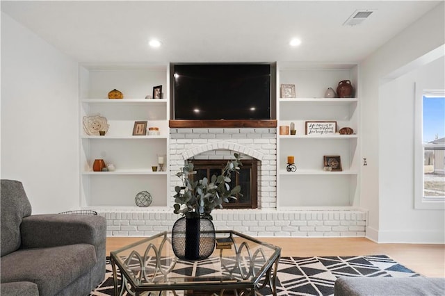 living room featuring built in features, baseboards, visible vents, wood finished floors, and a fireplace