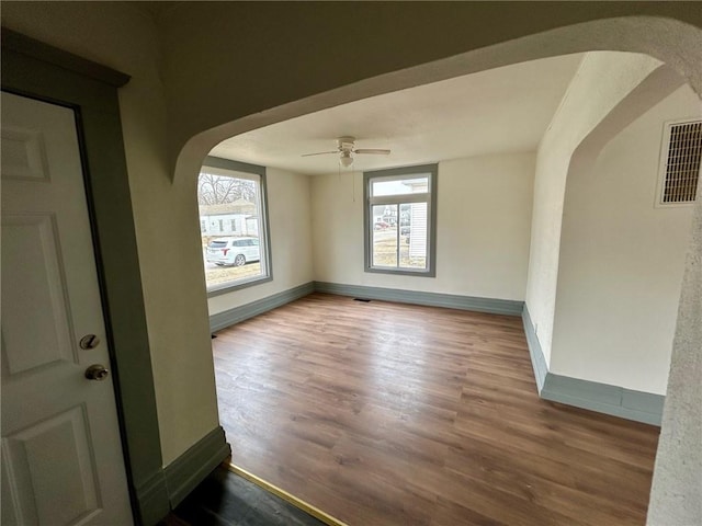 spare room with baseboards, visible vents, arched walkways, and wood finished floors