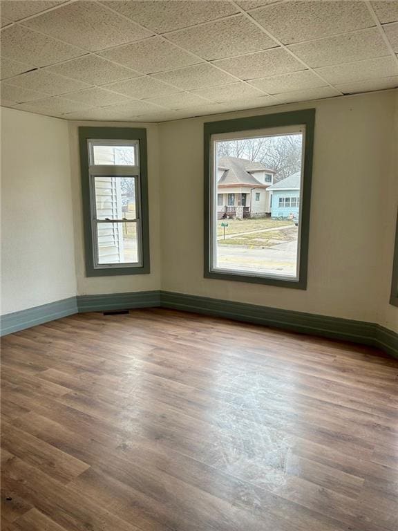 spare room featuring a drop ceiling, wood finished floors, and baseboards