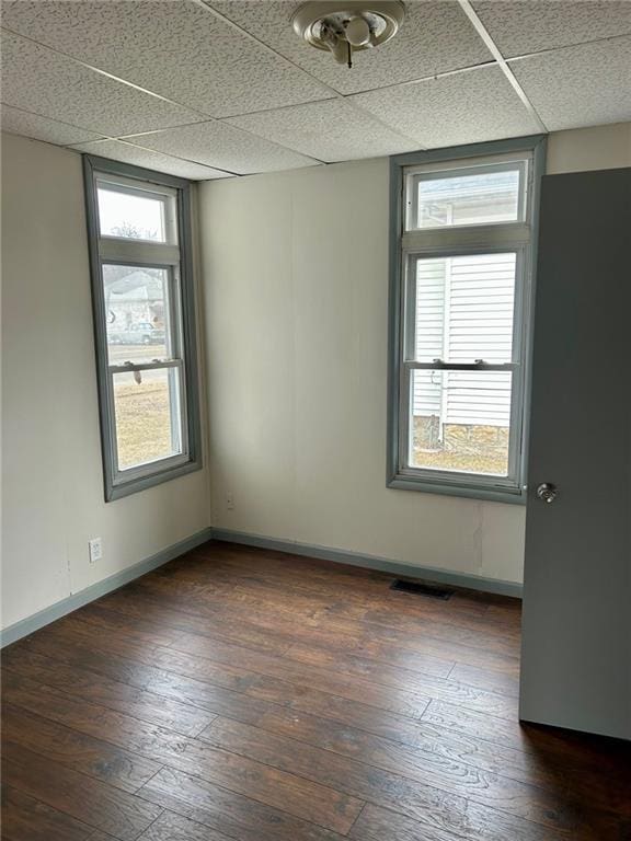 spare room with dark wood-type flooring, a paneled ceiling, visible vents, and baseboards