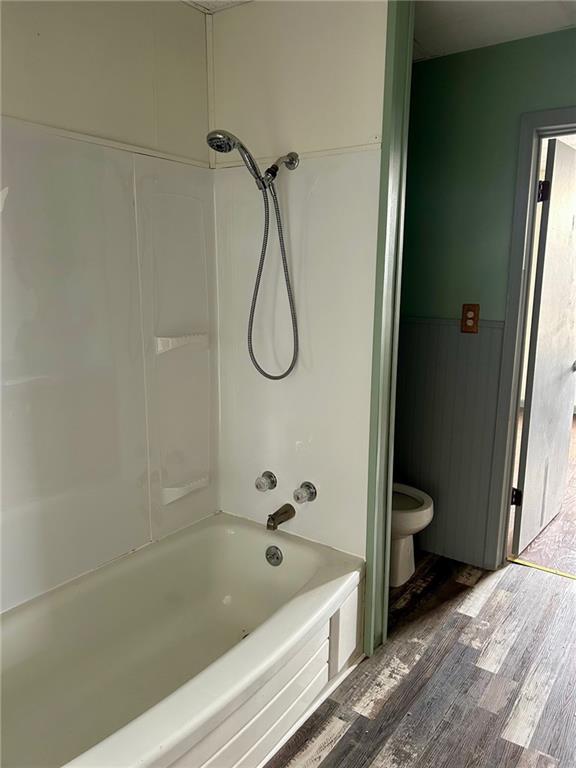 bathroom featuring a wainscoted wall, shower / bathing tub combination, wood finished floors, and toilet