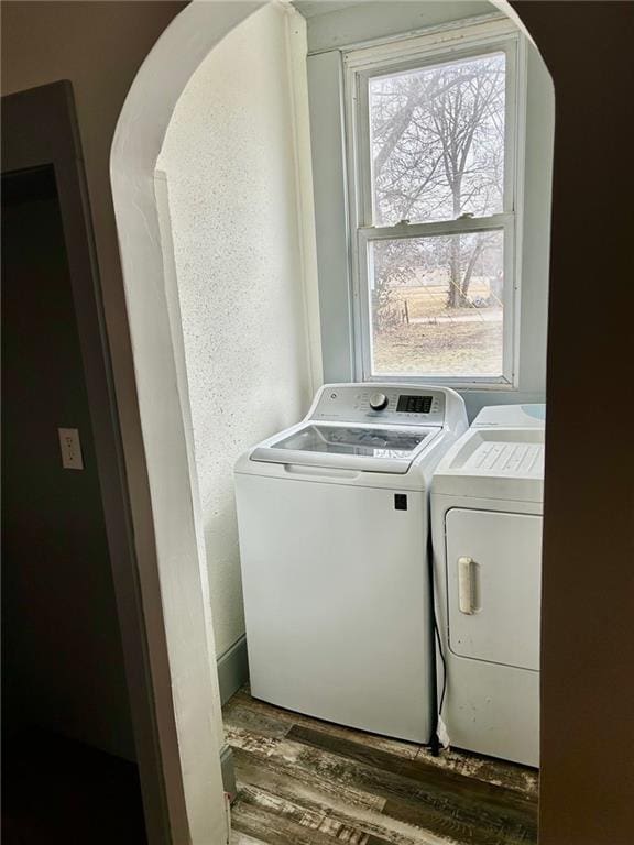 clothes washing area featuring laundry area, washing machine and dryer, arched walkways, and wood finished floors