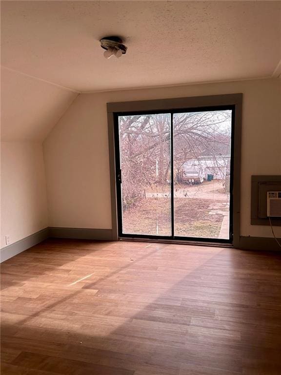 additional living space with a wall unit AC, a textured ceiling, vaulted ceiling, and wood finished floors