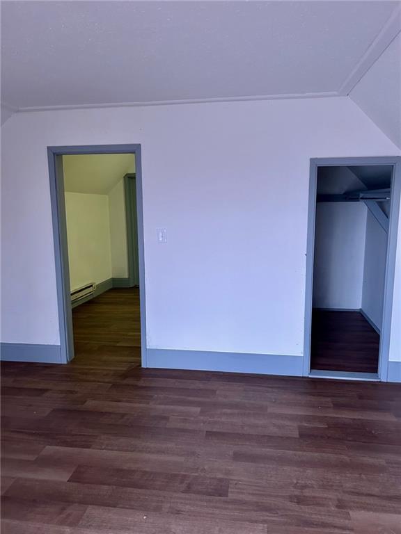 additional living space with a baseboard heating unit, lofted ceiling, baseboards, and wood finished floors