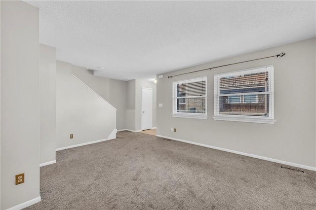 empty room with carpet, visible vents, baseboards, and a textured ceiling