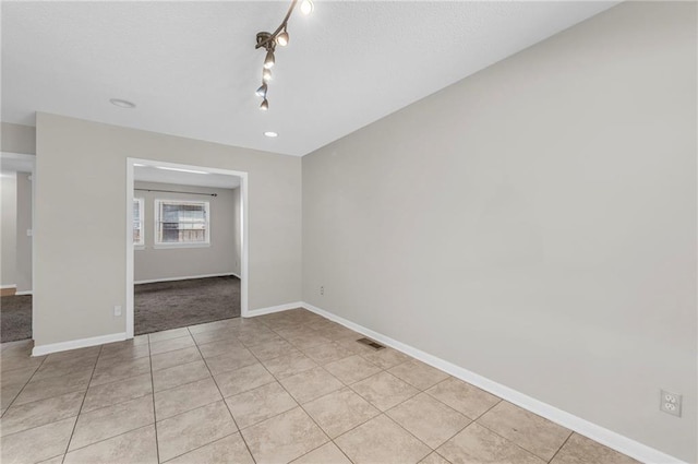 empty room featuring light tile patterned floors, a textured ceiling, visible vents, and baseboards