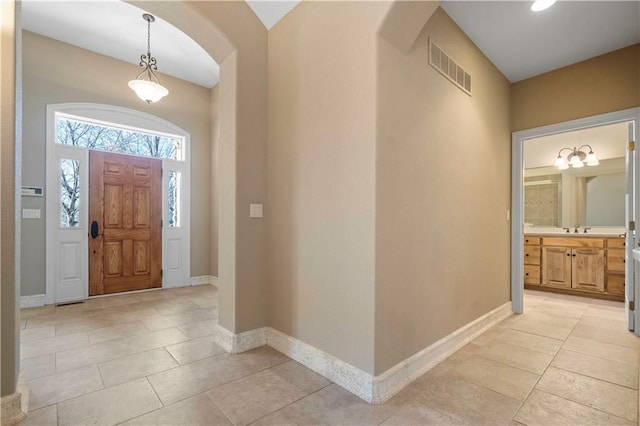 foyer entrance featuring arched walkways, light tile patterned flooring, visible vents, and baseboards