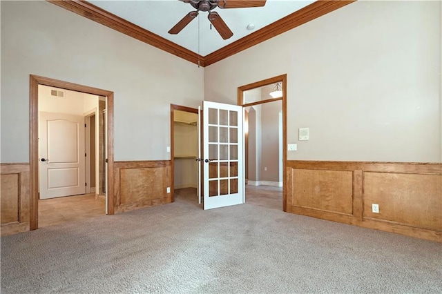 unfurnished room with a wainscoted wall, ceiling fan, carpet, crown molding, and french doors