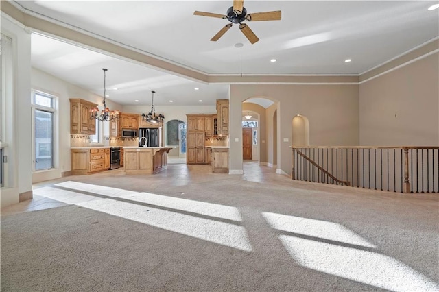 unfurnished living room featuring light carpet, recessed lighting, baseboards, arched walkways, and ceiling fan with notable chandelier