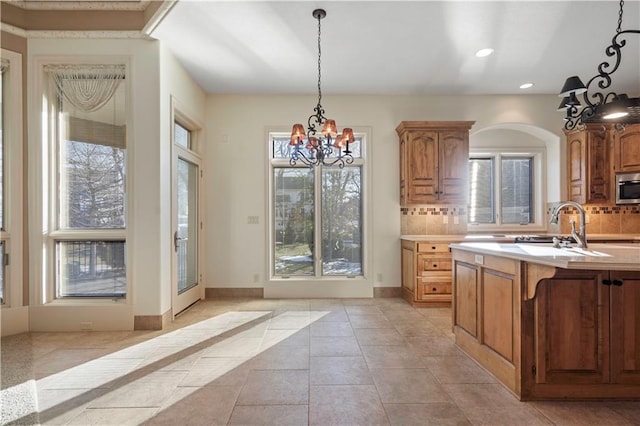 kitchen featuring a sink, light countertops, backsplash, stainless steel microwave, and pendant lighting