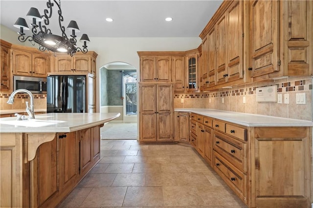 kitchen with arched walkways, light countertops, backsplash, freestanding refrigerator, and stainless steel microwave