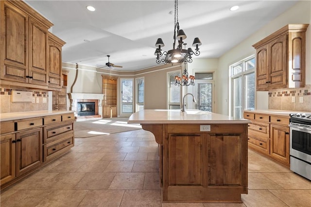 kitchen with a kitchen island with sink, a fireplace, a sink, light countertops, and stainless steel electric range oven