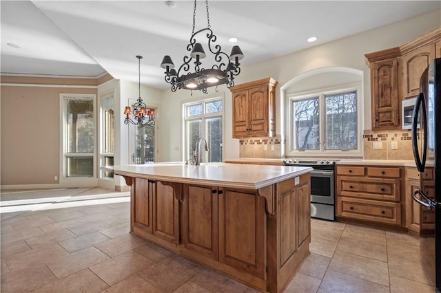 kitchen with plenty of natural light, appliances with stainless steel finishes, a kitchen island with sink, light countertops, and backsplash