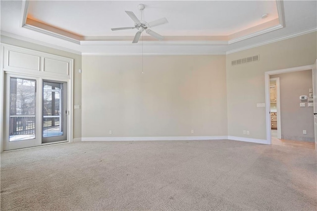 empty room featuring light carpet, a tray ceiling, visible vents, and crown molding