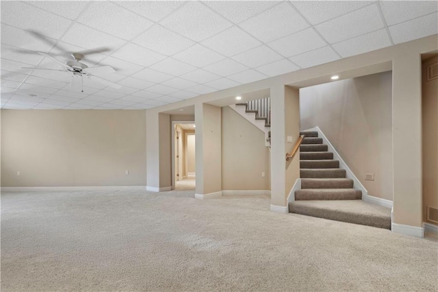 finished below grade area featuring stairs, a drop ceiling, carpet flooring, and baseboards