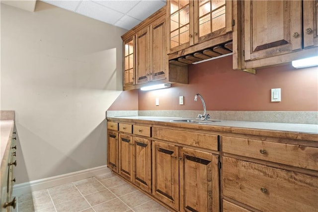 kitchen featuring a drop ceiling, brown cabinets, light countertops, a sink, and light tile patterned flooring