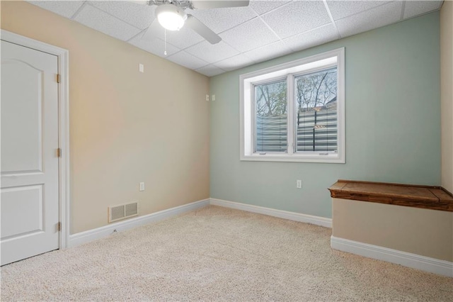 carpeted spare room featuring visible vents, ceiling fan, a drop ceiling, and baseboards