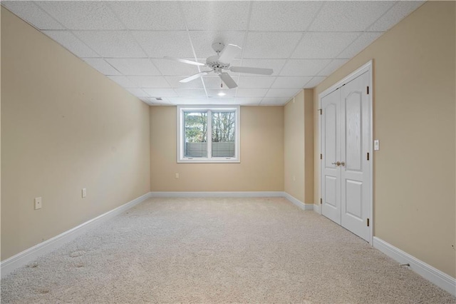 spare room featuring baseboards, a drop ceiling, a ceiling fan, and light colored carpet