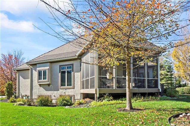 back of property with a lawn, a sunroom, and stucco siding