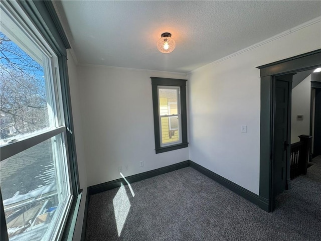 empty room featuring baseboards, dark carpet, a textured ceiling, and ornamental molding