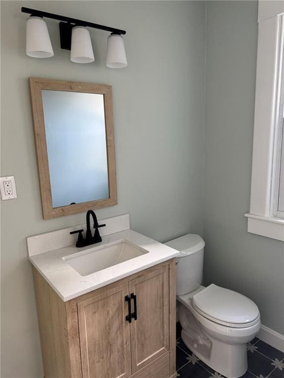 half bathroom featuring tile patterned floors, vanity, toilet, and baseboards