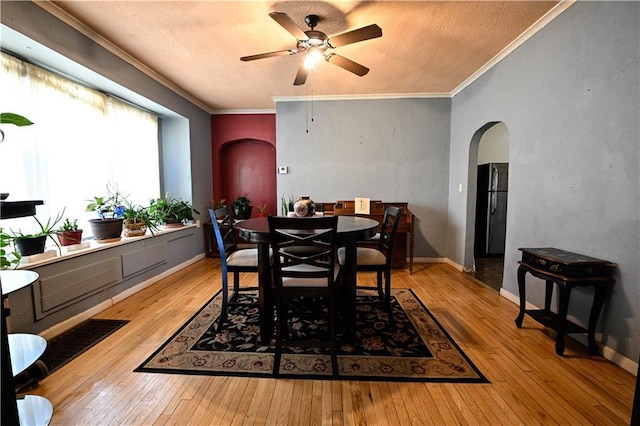 dining area featuring arched walkways, crown molding, and hardwood / wood-style floors