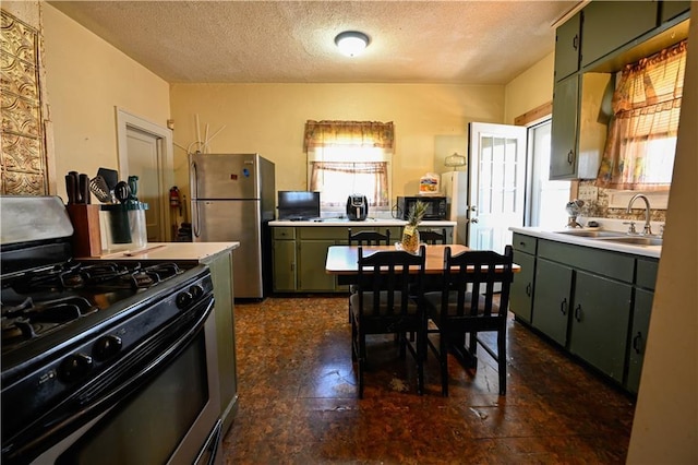 kitchen featuring a sink, range with gas stovetop, freestanding refrigerator, light countertops, and green cabinetry