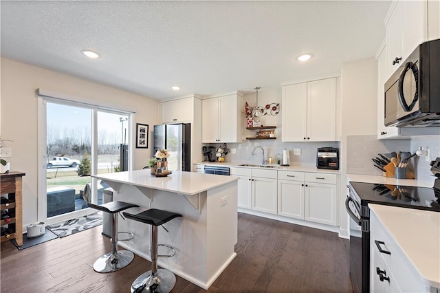 kitchen with a sink, a kitchen island, white cabinets, black appliances, and dark wood-style flooring