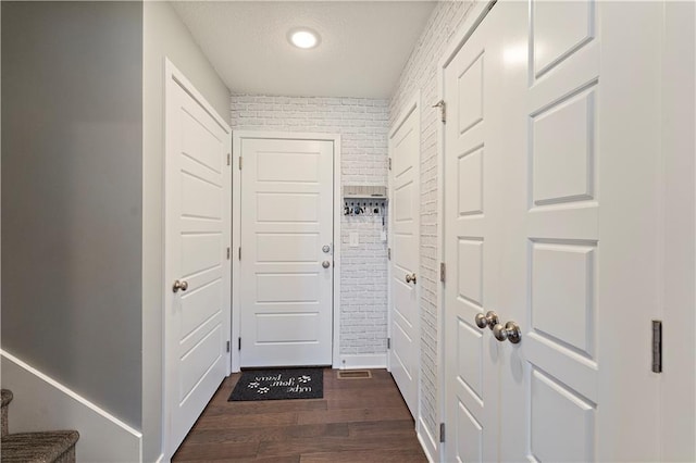 doorway to outside featuring dark wood-style floors, a textured ceiling, and brick wall