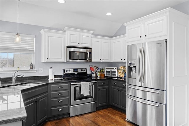 kitchen with dark wood-type flooring, dark stone counters, appliances with stainless steel finishes, white cabinetry, and a sink