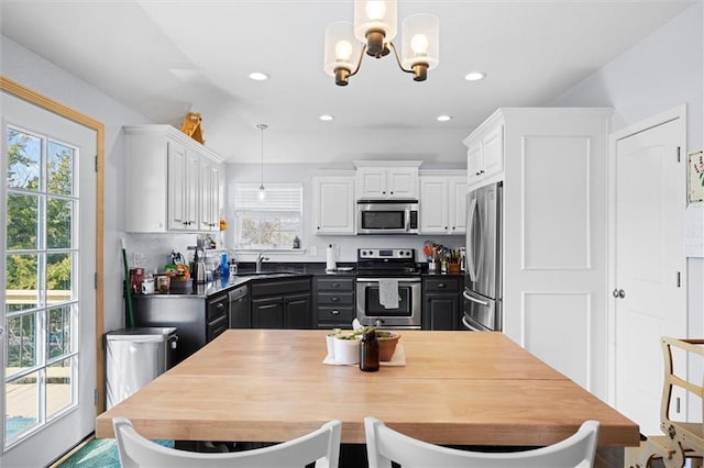 kitchen featuring pendant lighting, stainless steel appliances, a notable chandelier, white cabinetry, and a sink