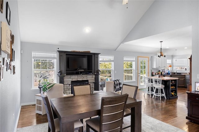 dining room featuring dark wood finished floors, a stone fireplace, lofted ceiling, and a wealth of natural light