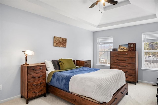 bedroom featuring a ceiling fan, a tray ceiling, light colored carpet, and baseboards